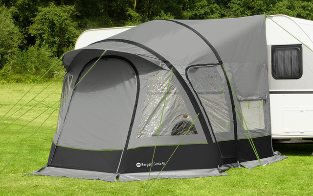 Weißer Wohnwagen mit grauem Vorzelt auf grüner Wiese vor Bäumen und blauem Himmel