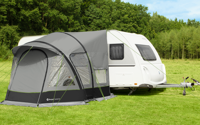 White caravan with gray awning on green grass in front of trees and blue sky