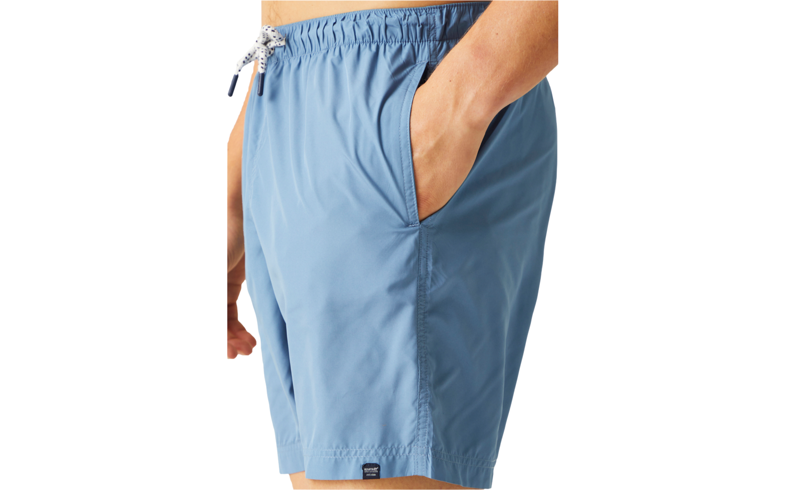 Vue partielle d'une personne de la taille au milieu de la cuisse, short de bain bleu clair avec cordon, une main dans la poche