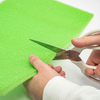 Mani che tagliano un pezzo di schiuma verde con delle forbici