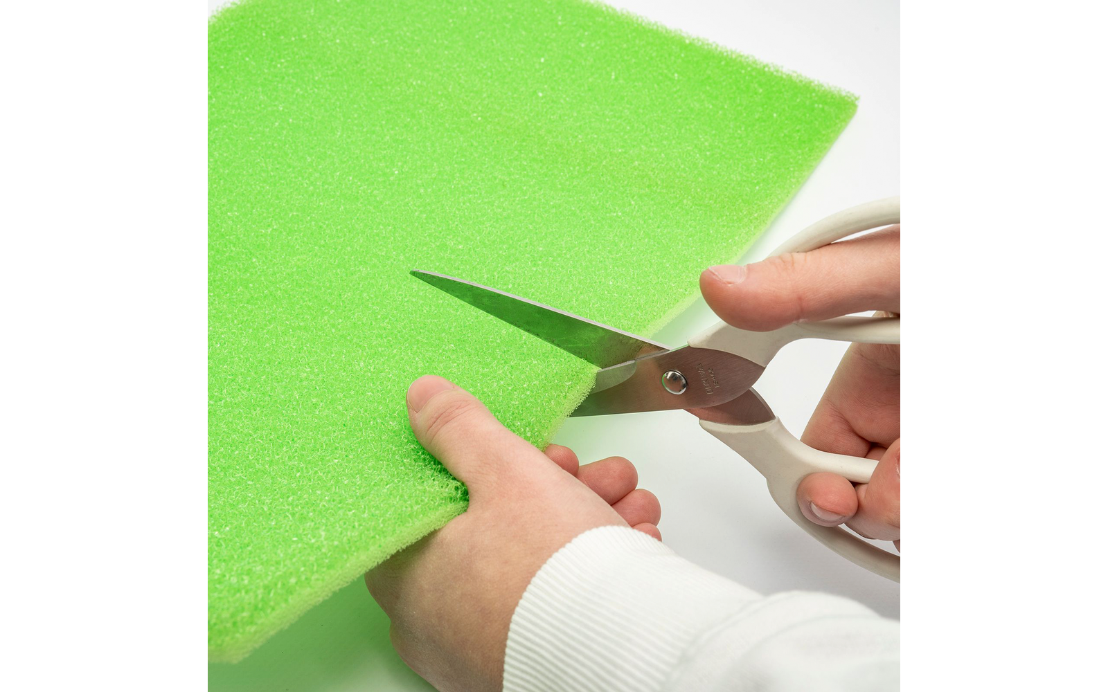 Mani che tagliano un pezzo di schiuma verde con delle forbici