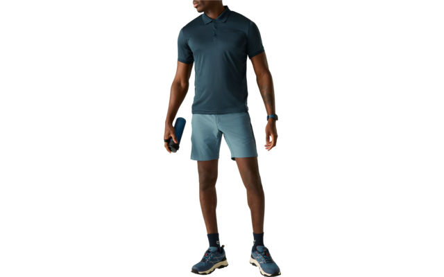 Person in dunkeltürkisfarbenem Poloshirt und hellblauen Shorts, hält eine blaue Flasche, trägt dunkle Socken und Sportschuhe