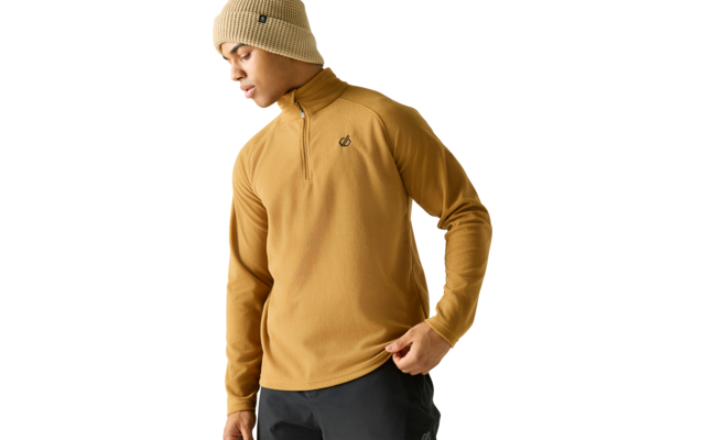 Persoon met beige gebreide muts en mosterdkleurige fleece met halve rits en klein borstlogo, kijkt naar beneden, linkerhand houdt zoom vast