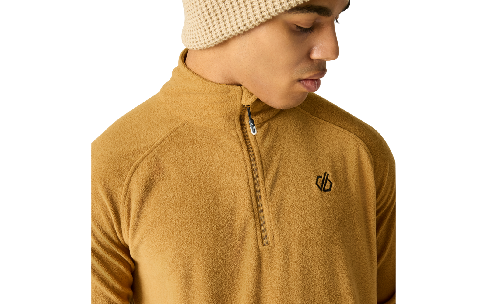 Persoon met beige gebreide muts en mosterdgele fleece met korte rits en klein zwart logo op de linkerborst, kijkt omlaag naar rechts, lichte achtergrond