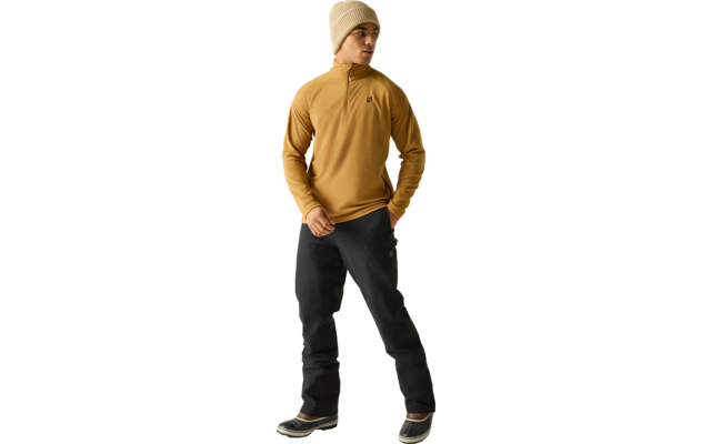 Staande persoon in mosterdkleurige trui met korte rits, beige gebreide muts, zwarte broek en zwarte winterlaarzen met lichte zolen, kijkt opzij