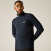 Mann mit kurzem Haar und kurzem Bart, trägt dunkelblauen Fleecepullover mit kurzem Reißverschluss, Hände hinter dem Rücken, heller neutraler Hintergrund