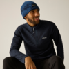 Sitzender Mann mit blauer Strickmütze und dunkelblauem Pullover mit kurzem Reißverschluss, lächelnd und zur Seite schauend