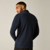 Person von hinten, Kopf nach links gedreht, trägt marineblauen Pullover und dunkle Hose, heller einfarbiger Hintergrund