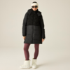 Person steht vor beigem Hintergrund, trägt schwarze gesteppte Kapuzen-Winterjacke mit Fleecebesatz, bordeauxfarbene Leggings, weiße hohe Winterstiefel, weißes Stirnband und schwarze Sonnenbrille