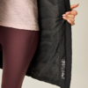 Teilansicht einer Person, die eine schwarze gesteppte Jacke aufhält; darunter sichtbares rosafarbenes Oberteil und burgunderfarbene Leggings; Innenseite der Jacke mit Pflegekennzeichnungen; Hand mit hell lackierten Nägeln