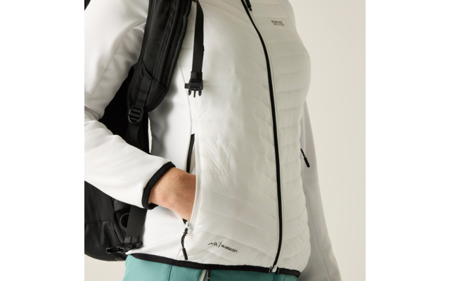 Oberkörper einer Person in weißer gesteppter Jacke mit schwarzem Reißverschluss, rechte Hand in Seitentasche, schwarzer Rucksackriemen über der Schulter, türkisfarbene Hose sichtbar