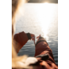 Rückenansicht einer Person in orangefarbener Jacke, die mit beiden Händen eine Schnur über ruhigem Wasser mit heller Sonnenreflexion hält