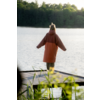 Person mit orangefarbenem Mantel steht mit dem Rücken zur Kamera auf einem Holzsteg am See; im Hintergrund Wald