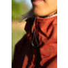 Nahaufnahme von Mund, Kinn und Hals; rote Jacke mit Reißverschluss und schwarzem Kordelzug; weißer Rüschenkragen; unscharfer grüner Hintergrund; Sonnenschein auf der Haut
