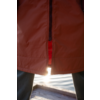 Orange Jacke mit unten leicht geöffnetem Reißverschluss, rote Innenlage sichtbar, dunkle Hosen, Holzsteg und Wasser mit Sonnenreflexion zwischen den Beinen