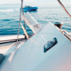 Schräg liegendes Sektglas auf einem schwarzen Untersetzer auf weißer Bootskante, Meer und Motorboot im Hintergrund
