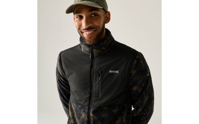 Nahaufnahme einer lächelnden Person mit Baseballcap, Bart und Fleecejacke mit Reißverschluss und Logo