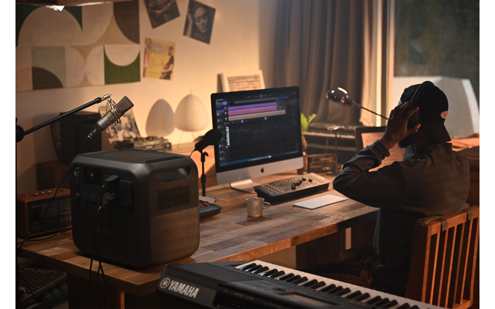 Person sitzt an einem Schreibtisch mit Computern und Musikequipment in einem dunklen Raum