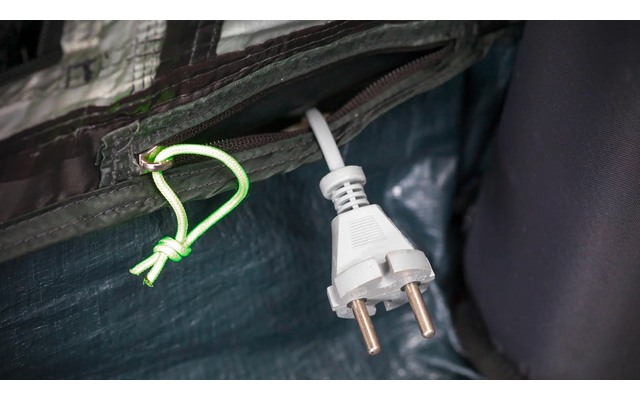 Weißer Stecker mit zwei runden Metallstiften an weißem Kabel, hängt aus einer dunklen Stofftasche mit grünem Reißverschlusszug