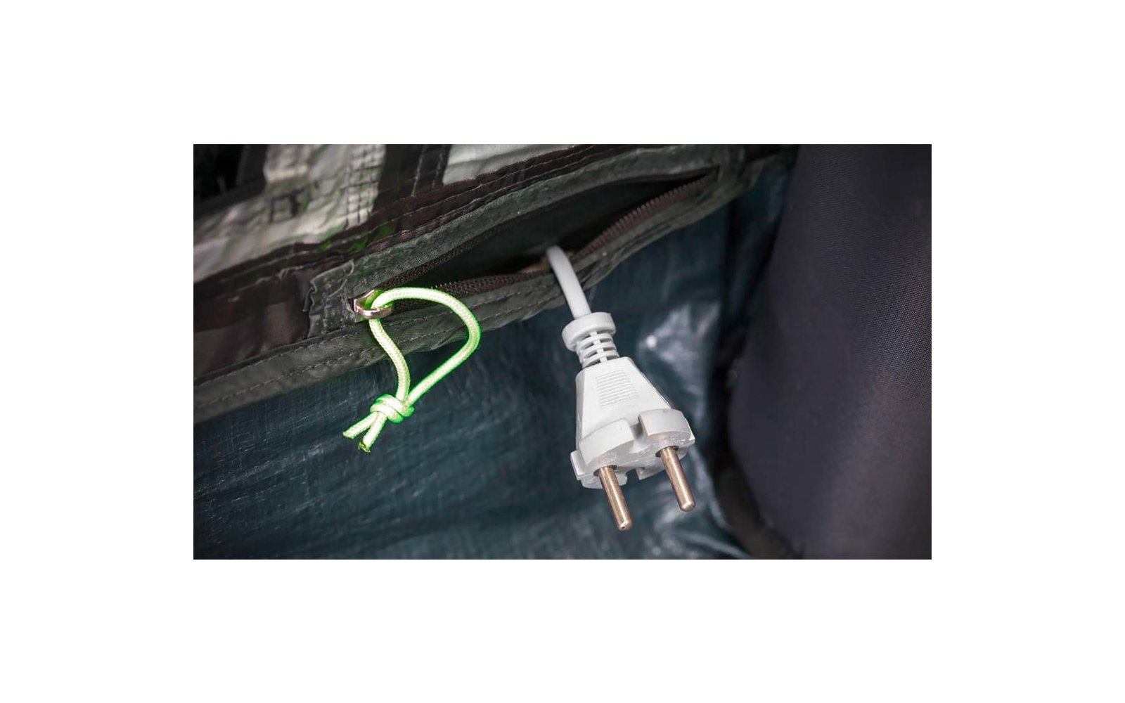 Weißer Netzstecker mit zwei runden Metallstiften an weißem Kabel neben grüner Schnur mit Knoten vor dunklem Stoff