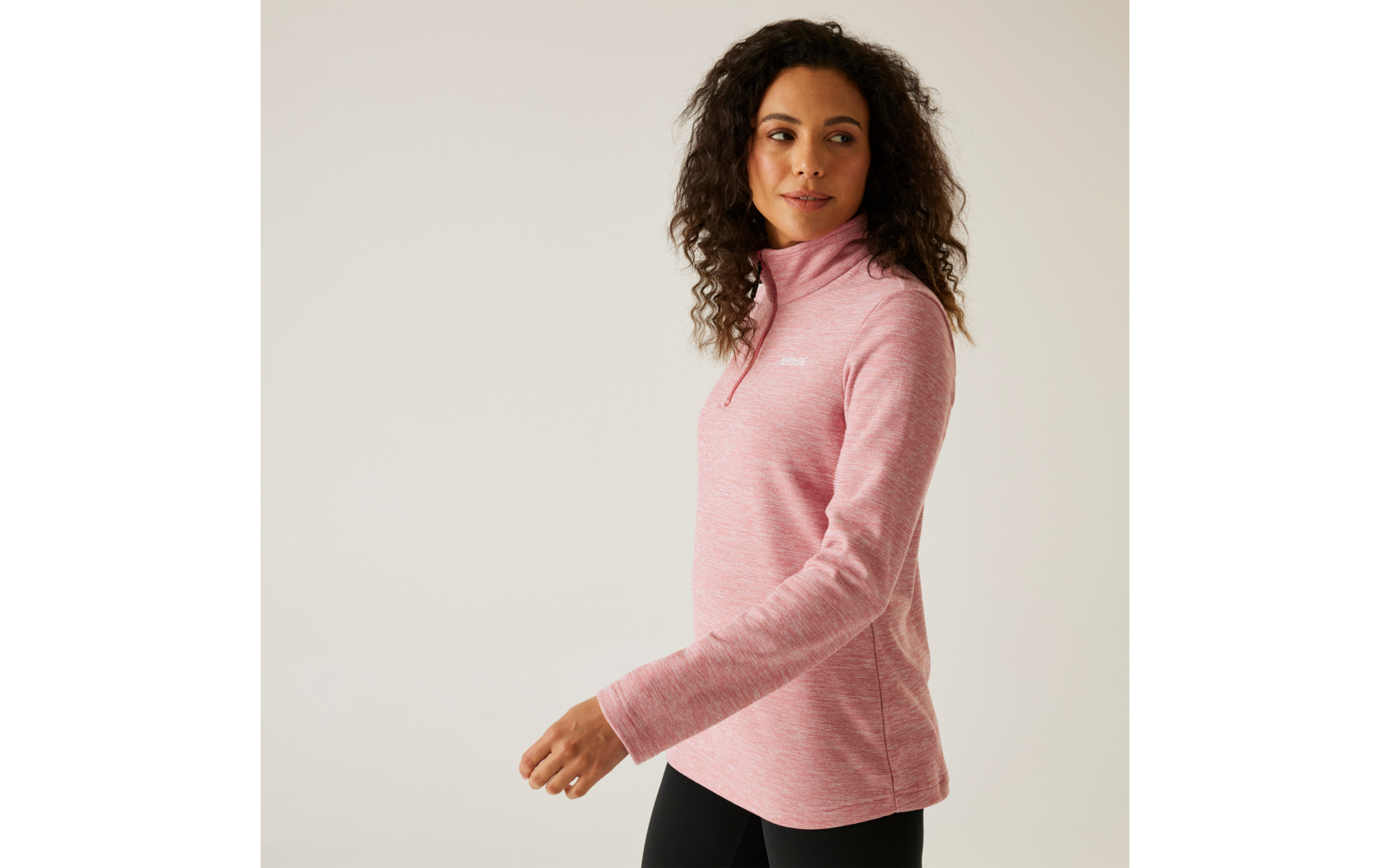 Frau mit lockigem Haar trägt einen rosa Pullover und blickt zur Seite