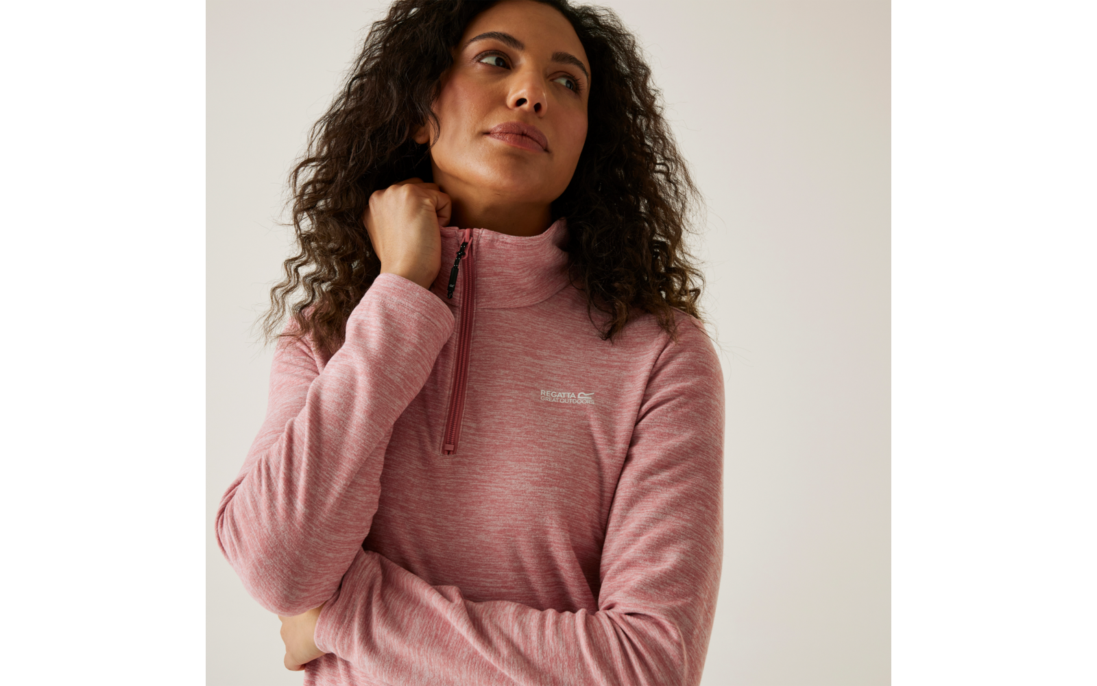 Frau mit lockigem Haar trägt einen rosa Pullover und schaut nach rechts oben