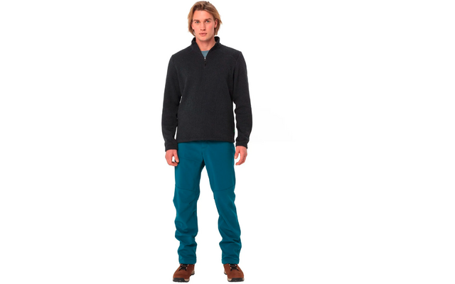 Ein Mann steht, trägt einen schwarzen Pullover, blaue Hose und braune Schuhe