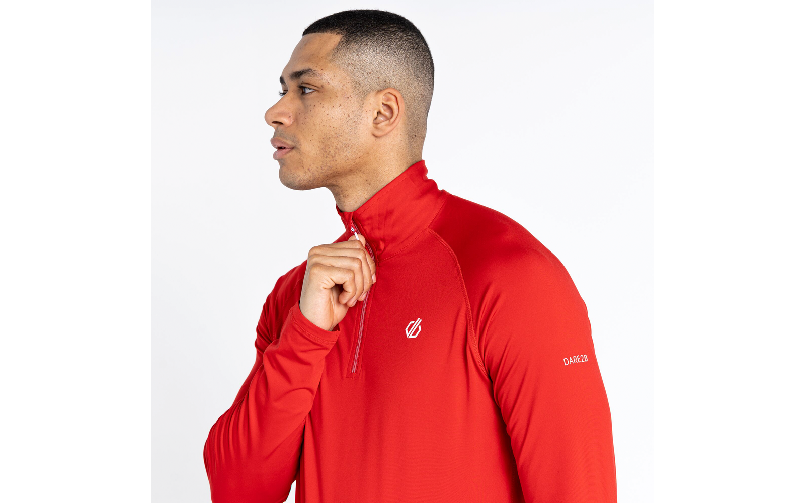 Portret van een man in een rood shirt met lange mouwen, die naar links kijkt en de rits van zijn shirt omhoog trekt