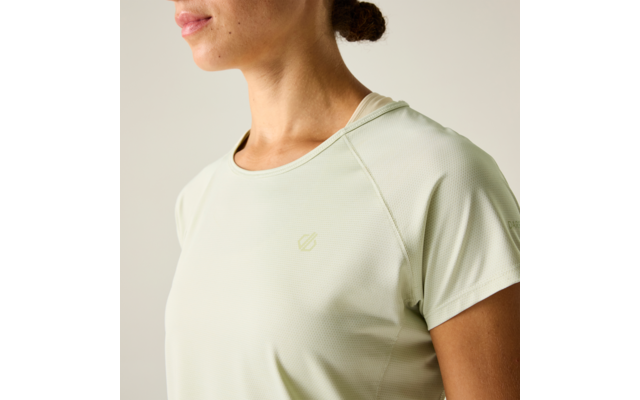 Nahaufnahme des Oberkörpers und des unteren Gesichts einer Person mit hellgrünem, kurzärmeligem Sportshirt und kleinem Logo auf der Brust; Haare zu einem niedrigen Dutt; heller einfarbiger Hintergrund