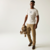 Mann mit weißem T-Shirt und hellbrauner Hose, der eine Jacke in der Hand hält