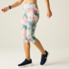 Lower torso and legs of a person wearing pastel floral capri leggings and navy sports shoes; right wrist with a fitness band; light background