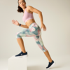 Person in a pink sports bra and pastel patterned capri leggings stepping with one foot onto a white block; navy sneakers, hair tied back, plain light background