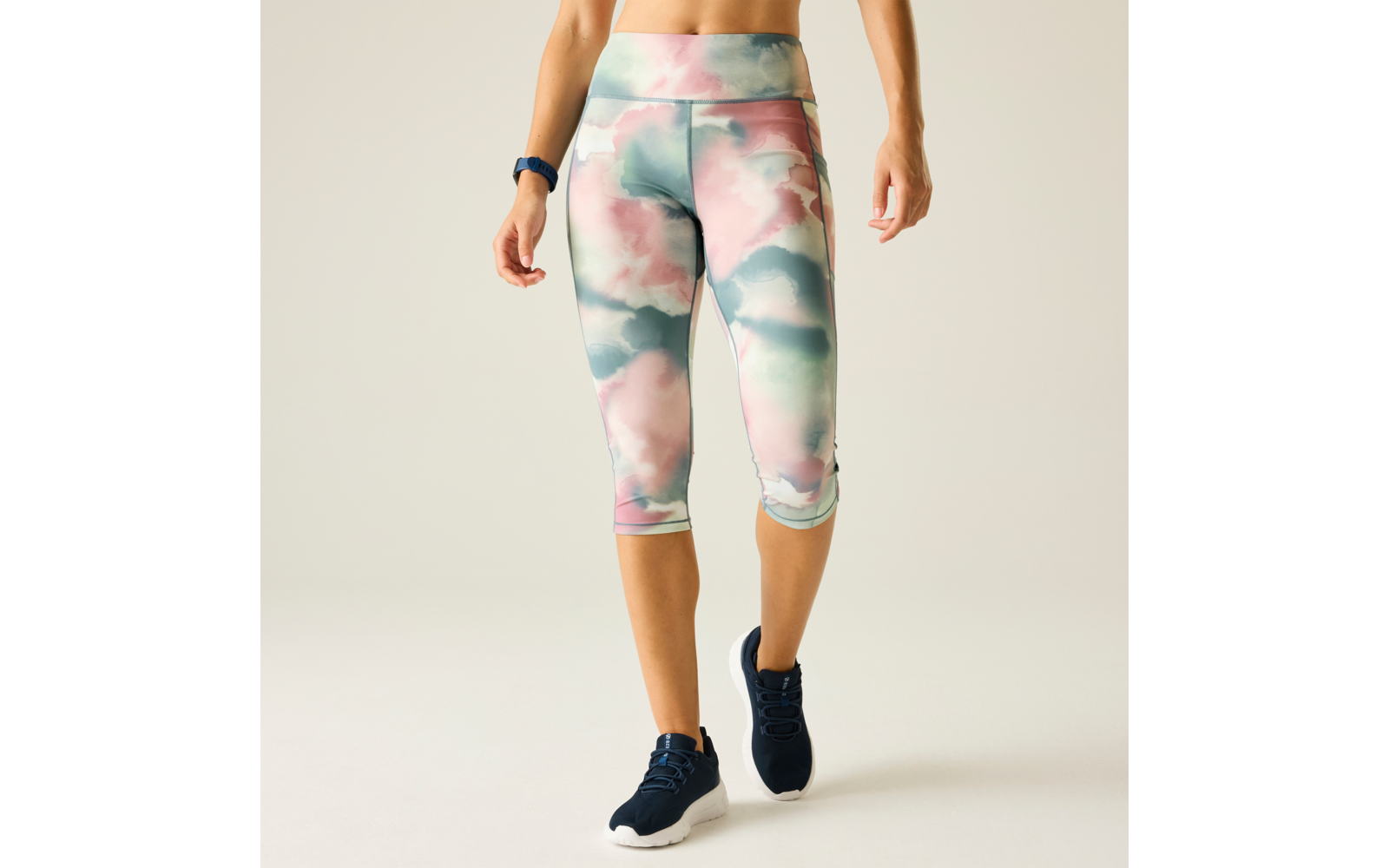 Lower body of a person from waist to feet wearing pastel cloud-pattern capri leggings, navy athletic shoes with white soles, and a fitness band on the wrist