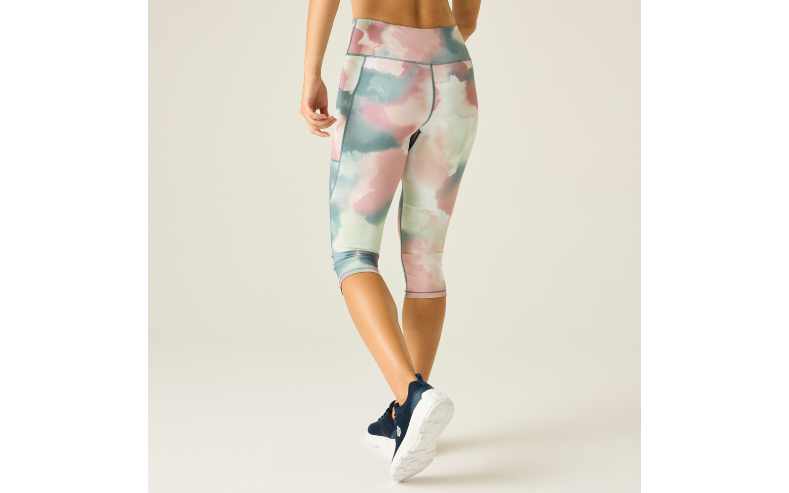 Person seen from behind wearing pastel watercolor capri leggings and navy sneakers on a light background