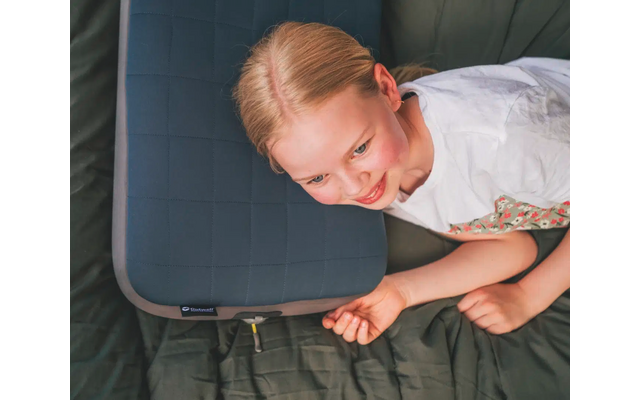 Bambino con capelli biondi sdraiato su una coperta verde scuro che tiene un cuscino da seduta blu scuro