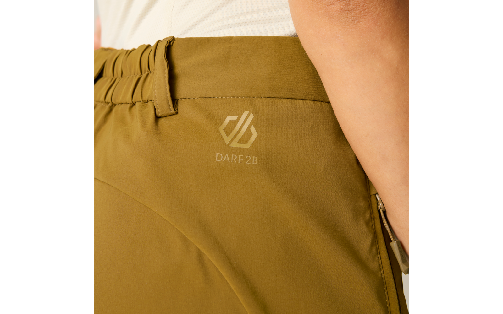 Primer plano de pantalones verde oliva con cintura elástica, cremallera lateral, logo impreso 'DARF2B' y brazo parcialmente visible con prenda blanca