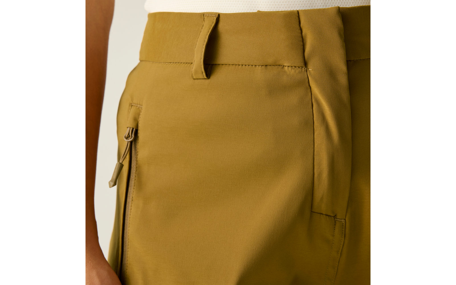 Acercamiento de la cintura con pantalones color mostaza, bolsillo con cremallera, trabillas y top blanco