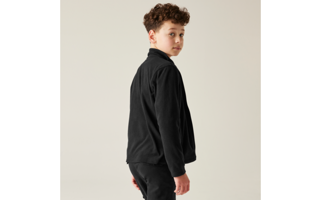 Ragazzo in piedi di spalle alla fotocamera, guarda oltre la spalla, indossa giacca e pantaloni neri, sfondo chiaro uniforme