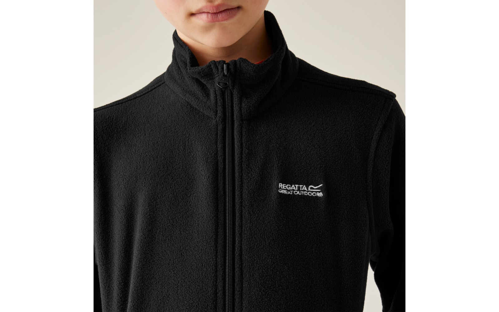 Parte superiore del corpo di una persona con pile nero, cerniera chiusa e piccolo logo bianco "Regatta Great Outdoors" sul petto sinistro; parte inferiore del viso (bocca e mento) visibile