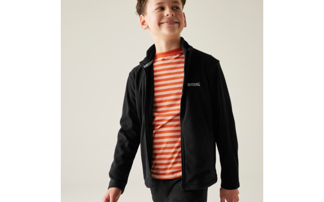 Ragazzo con T-shirt a righe arancione e bianca e giacca nera con zip, guarda verso destra, sfondo chiaro