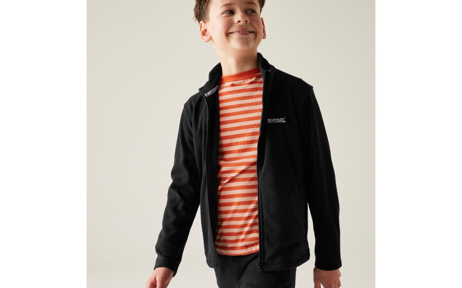 Ragazzo con T-shirt a righe arancione e bianca e giacca nera con zip, guarda verso destra, sfondo chiaro