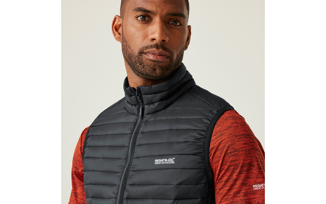 Mann mit schwarzen, leicht gewellten kurzen Haaren trägt eine schwarze gesteppte Weste und ein rotes Langarmshirt