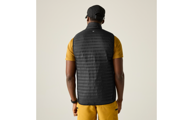 Person von hinten mit schwarzer gesteppter Weste, gelbem Kurzarmshirt, gelber Hose, schwarzer Kappe und Armbanduhr, heller einfarbiger Hintergrund