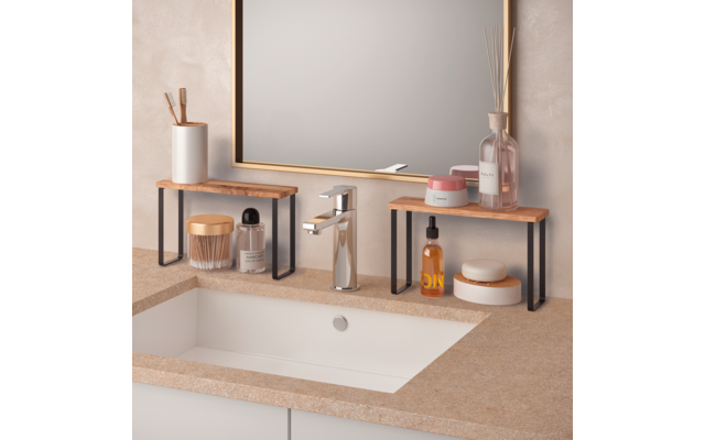 Waschbecken mit weißer Einbauwanne, verchromtem Wasserhahn, rechteckigem Spiegel mit goldfarbenem Rahmen, zwei hölzerne Ablagen mit schwarzen Metallbeinen auf der Arbeitsplatte, darauf Zahnbürstenhalter, Cremedosen, Flaschen und Diffusor mit Duftstäb