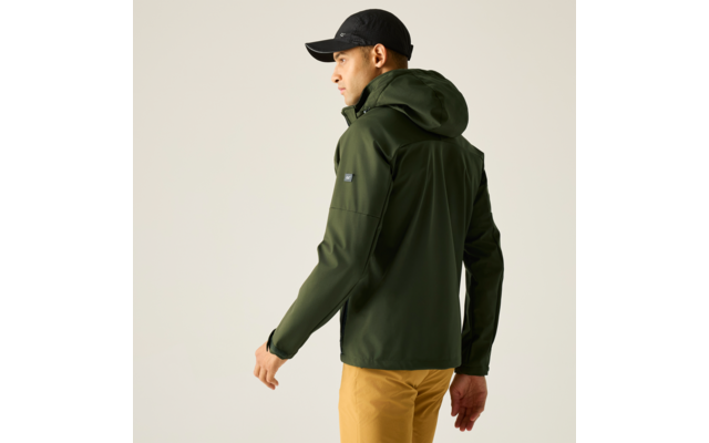 Person von hinten, leicht seitlich, trägt dunkelgrüne Kapuzenjacke, senfgelbe Hose und schwarze Kappe, heller Hintergrund