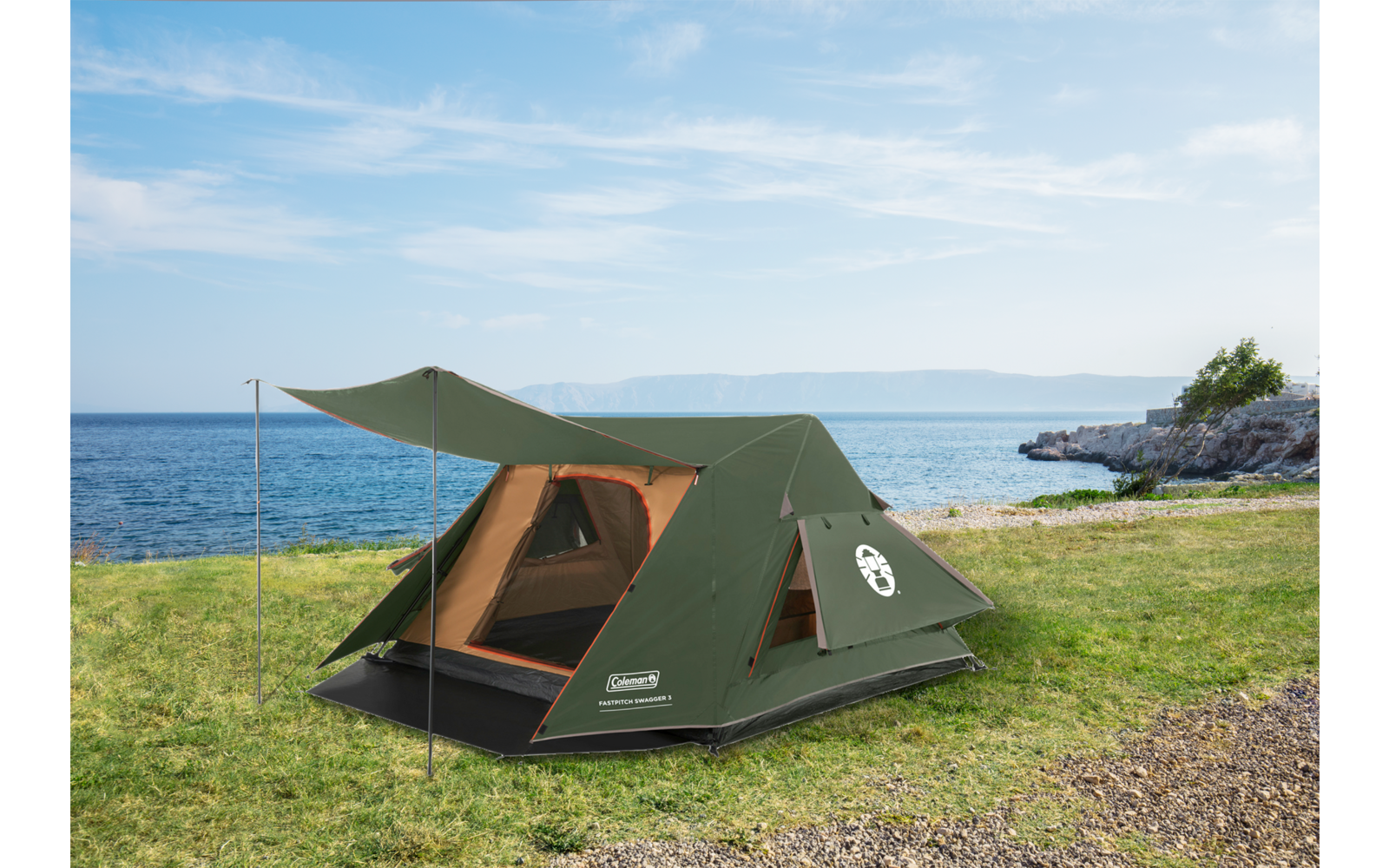 Grünes Zelt mit geöffnetem Eingang auf Gras nahe felsiger Küste und Meer unter teilweise bewölktem Himmel