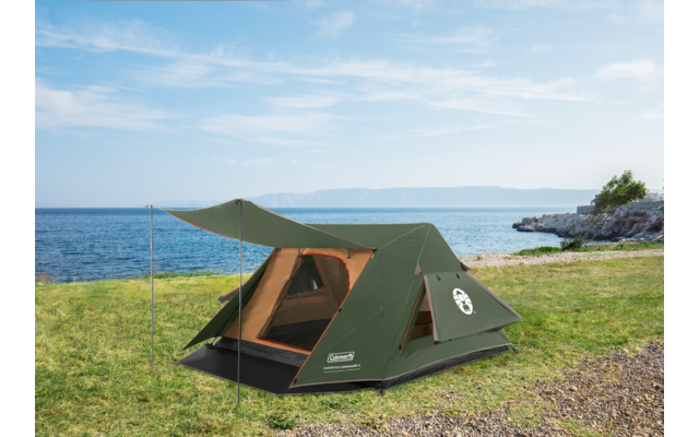 Green tent with open entrance on grass by a rocky shoreline and the sea under a partly cloudy sky
