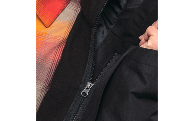 Nahaufnahme eines Reißverschlusses an einer schwarzen Jacke, darunter ein kariertes orange-rotes Hemd und eine Hand an der Jackenöffnung