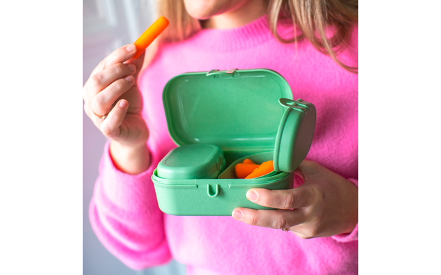 Personne en pull rose tient une boîte plastique verte ouverte contenant des bouchons d’oreille en mousse orange; une main tient un bouchon près de la bouche; seul le bas du visage est visible