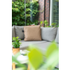 Grijze bank met beige kussen, kleine ronde tafel met plantenpot en kopje, glazen wand, bakstenen muur en groene planten, onscherpe bladeren op de voorgrond